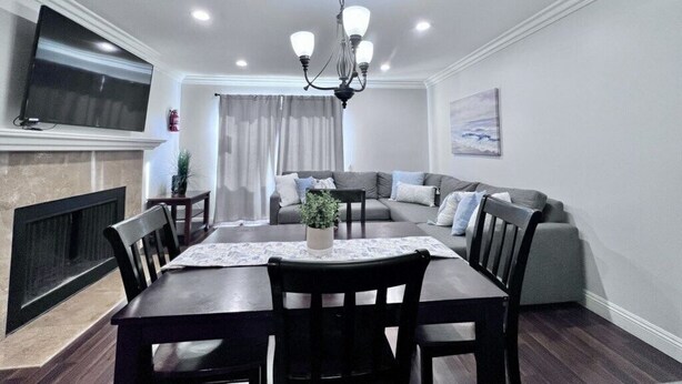 Un comedor con mesa, sillas, una araña, televisor y sofá.