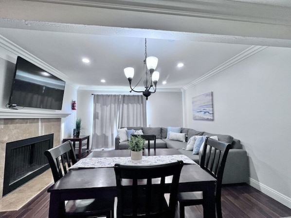 A dining area with a table, chairs, a chandelier, a television, and a sofa.