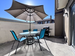 An outdoor patio with a round table, four chairs, a large umbrella, and a barbecue grill.
