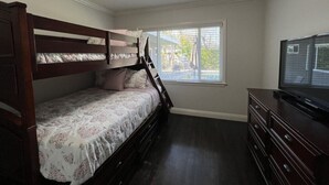 Un dormitorio con literas, cómoda, televisor y ventana con persianas.