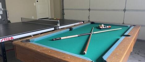 A pool table with a TIGA table, pool cues, and balls in a room with a garage door and a white door.