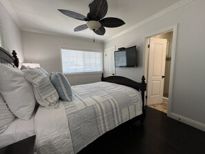 Een slaapkamer met een bed, een plafondventilator, een televisie en een deur.