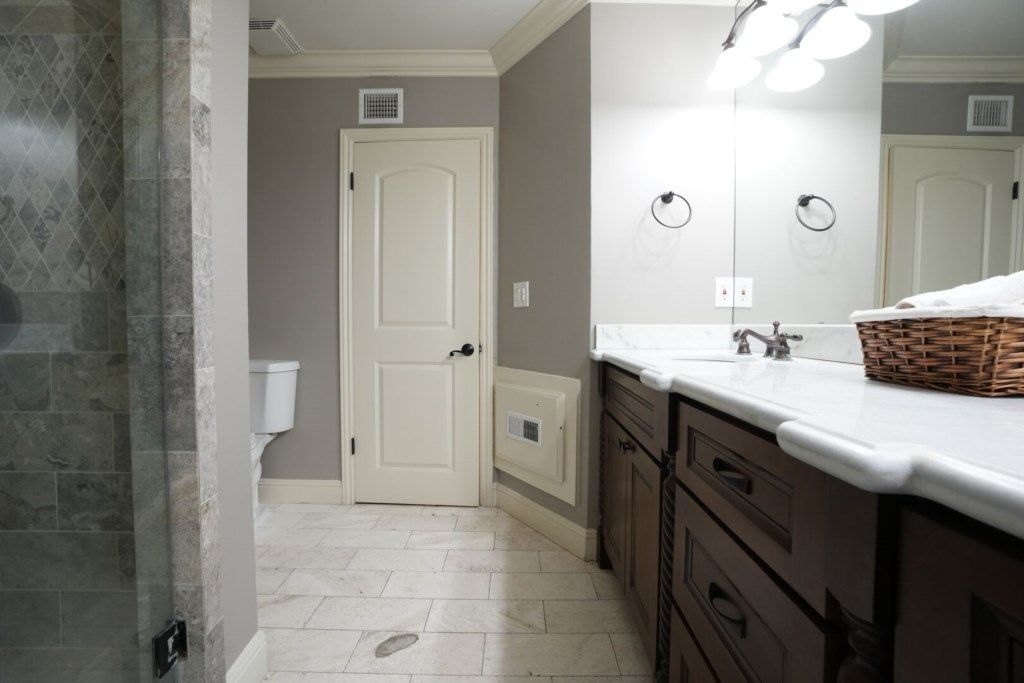 A bathroom with a white door, a white sink, a mirror, and a basket on the counter.