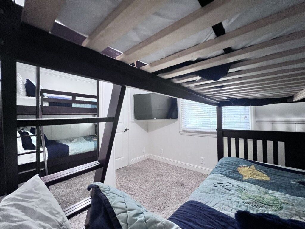 Een slaapkamer met een stapelbed, een televisie aan de muur, een raam en een deur.