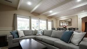 A living room with a sectional sofa, a dark wooden coffee table, and a dining area with a mirror and chairs. - Incredible Estate 5 Bedrooms 3 Bathroom W/resort Style Rock Pool & Jacuzzi (Fullerton)