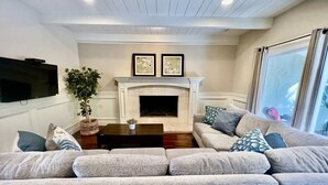 A living room with a fireplace, a television, and a large window. - Incredible Estate 5 Bedrooms 3 Bathroom W/resort Style Rock Pool & Jacuzzi (Fullerton)