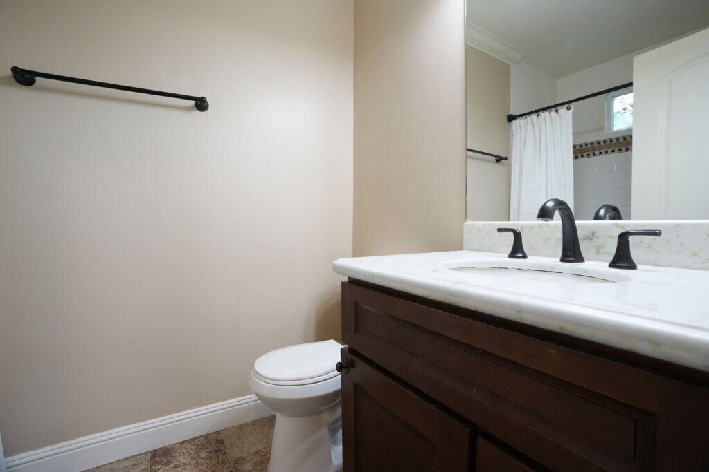 A bathroom with a toilet, a sink with a mirror above it, and a towel rack on the wall.