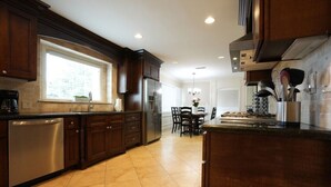 A kitchen with dark wooden cabinets, a stainless steel dishwasher, and a large window. - Incredible Estate 5 Bedrooms 3 Bathroom W/resort Style Rock Pool & Jacuzzi (Fullerton)