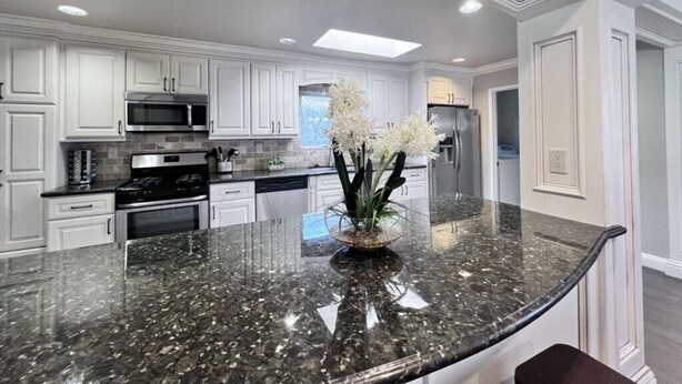 A kitchen with white cabinets, a granite countertop, a central island with a vase of flowers, and built-in appliances. - Fabulous 6 Bedroom , 4 Bath Pool W/jacuzzi Home (Orange)
