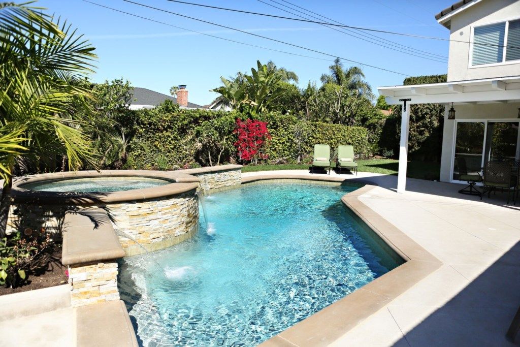A swimming pool with stone steps, a patio area, and a covered seating area.