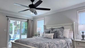 Un dormitorio con cama, ventilador de techo, mesita de noche y ventana.