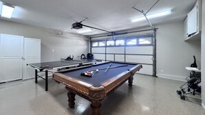 A pool table with balls, a ping pong table, and a ceiling-mounted projector in a room with a garage door and white cabinets. - Fabulous 6 Bedroom , 4 Bath Pool W/jacuzzi Home (Orange)