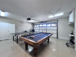 A pool table with balls, a ping pong table, and a ceiling-mounted projector in a room with a garage door and white cabinets. - Fabulous 6 Bedroom , 4 Bath Pool W/jacuzzi Home (Orange)