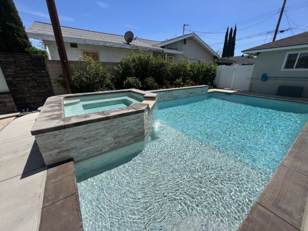 A swimming pool with a stone border and a small hot tub area.