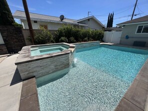 A swimming pool with a stone border and a small hot tub area. - Beautiful Remodel 3 Bedroom 2 Bathroom Home With Pool & Jacuzzi (Fullerton)