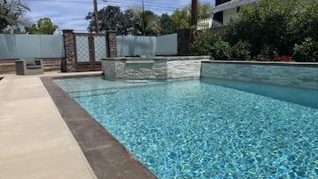 Une piscine bordée de pierres, un espace patio et une clôture blanche.