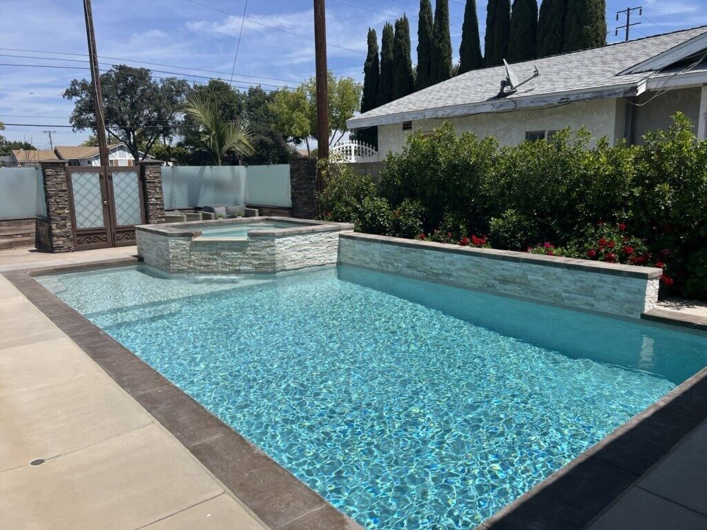 Ein Pool mit Steinbord, einer Steinmauer und einem überdachten Sitzbereich.