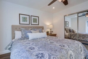 A bedroom with a large bed, a ceiling fan, a nightstand with a lamp, and two framed pictures on the wall. - Beautiful Remodel 3 Bedroom 2 Bathroom Home With Pool & Jacuzzi (Fullerton)