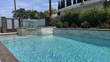 Une piscine aux eaux cristallines, bordée de pierres, entourée d’une clôture et de verdure.