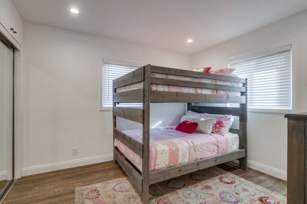 A bunk bed with a floral bedspread, a red pillow, and a patterned rug in a room with white walls and wooden flooring.