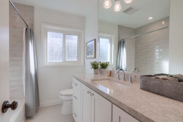 A bathroom with a toilet, a sink, a mirror, and a shower area. - Beautiful Remodel 3 Bedroom 2 Bathroom Home With Pool & Jacuzzi (Fullerton)