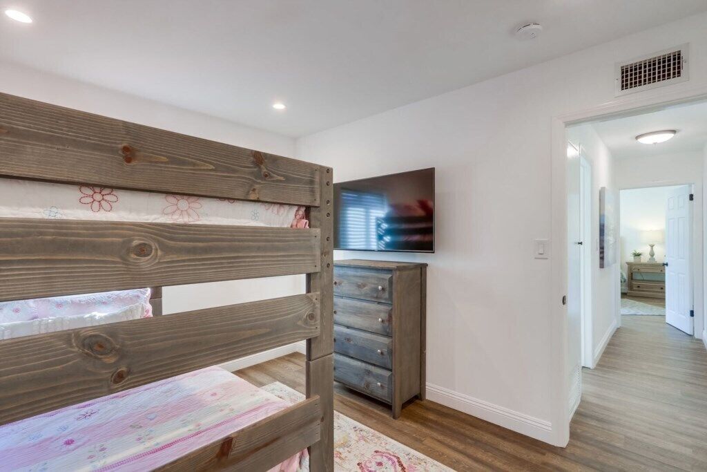 Ein Schlafzimmer mit einem hölzernen Etagenbett, einem Schminktisch, einem Flachbildfernseher und einem Flur, der in einen anderen Raum führt.