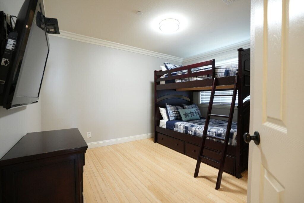 A room with a bunk bed, a dresser, and a television.