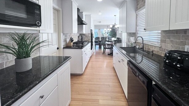 A modern kitchen with white cabinetry, a black countertop, and a central island. - 5 Bedroom 4 Bath Pool Home Near Disney (Anaheim)