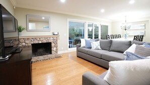 A living room with a stone fireplace, a grey sofa, and a television on a stand. - 5 Bedroom 4 Bath Pool Home Near Disney (Anaheim)