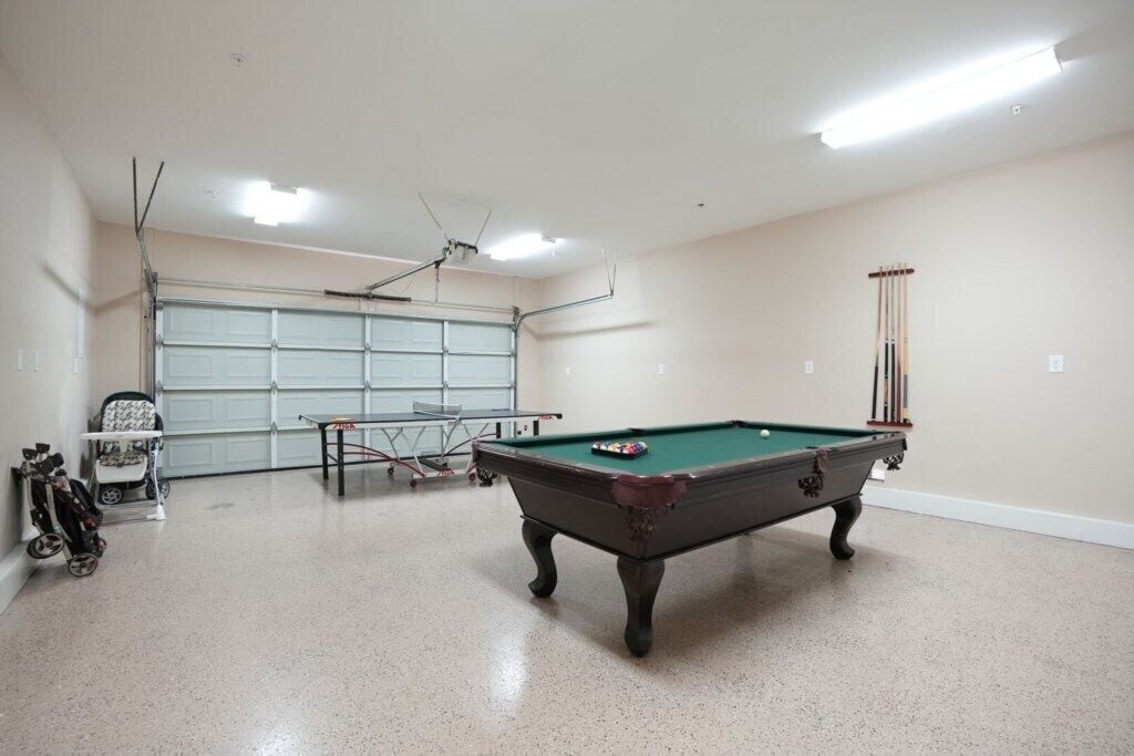 A pool table in a room with a ceiling fan, a stroller, and a garage door.