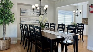 A dining room with a wooden table, black chairs, a chandelier, and a potted plant. - 5 Bedroom 4 Bath Pool Home Near Disney (Anaheim)