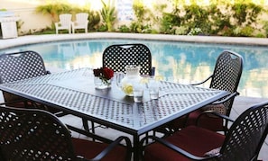 A round table with chairs, a pitcher, glasses, and a vase with flowers by a pool. - 5 Bedroom 4 Bath Pool Home Near Disney (Anaheim)
