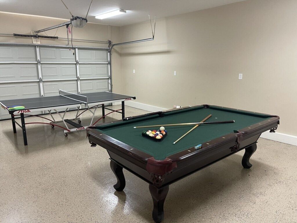 Une table de billard avec des billes et des queues, une table de ping-pong, et une porte de garage en arrière-plan.