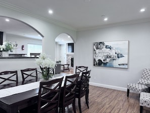 A dining area with a long table, dark wooden chairs, a vase with flowers, and a large black and white painting on the wall. - Lovely Anaheim Pool Home 1 Mile to Disney (Anaheim)