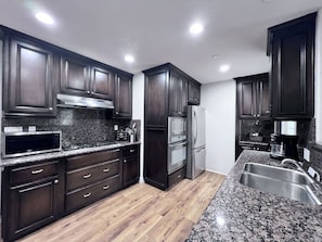 A modern kitchen with dark wood cabinets, stainless steel appliances, granite countertops, and a wooden floor. - Lovely Anaheim Pool Home 1 Mile to Disney (Anaheim)