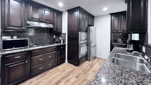 A modern kitchen with dark wood cabinets, stainless steel appliances, granite countertops, and a wooden floor. - Lovely Anaheim Pool Home 1 Mile to Disney (Anaheim)
