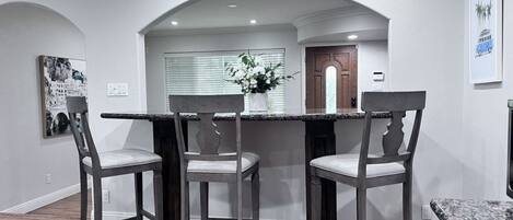 A dining area with a marble countertop, three chairs, and a vase of flowers.
