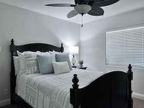 A bedroom with a bed, a ceiling fan, a bedside table with a lamp, and a window with blinds. - Lovely Anaheim Pool Home 1 Mile to Disney (Anaheim)