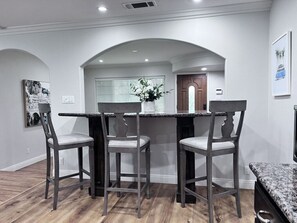 Un área de comedor con encimera de mármol, tres sillas y un jarrón con flores.