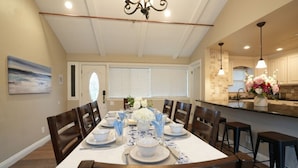 A dining area with a table set for four, a chandelier, and a kitchen in the background. - Snazzy 6 Bedroom 3 Bath Pool Home 1/2 Mile Walk to Disney (Anaheim)