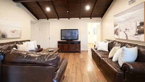 A living room with two leather sofas, a TV on a wooden stand, and artwork on the walls. - Snazzy 6 Bedroom 3 Bath Pool Home 1/2 Mile Walk to Disney (Anaheim)