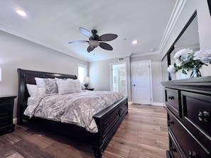A bedroom with a bed, dresser, ceiling fan, and a door.