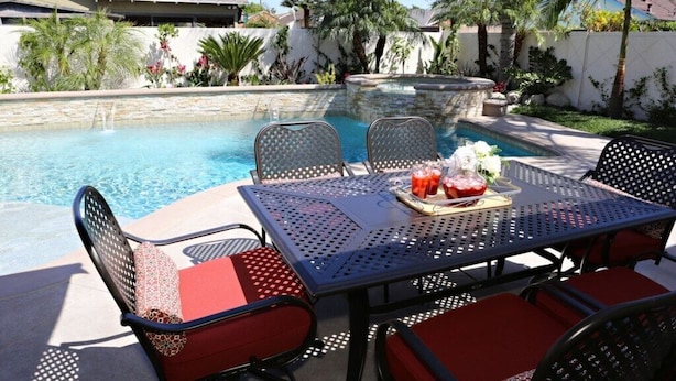 A poolside dining area with a table and chairs, a stone wall, and a pool. - Snazzy 6 Bedroom 3 Bath Pool Home 1/2 Mile Walk to Disney (Anaheim)