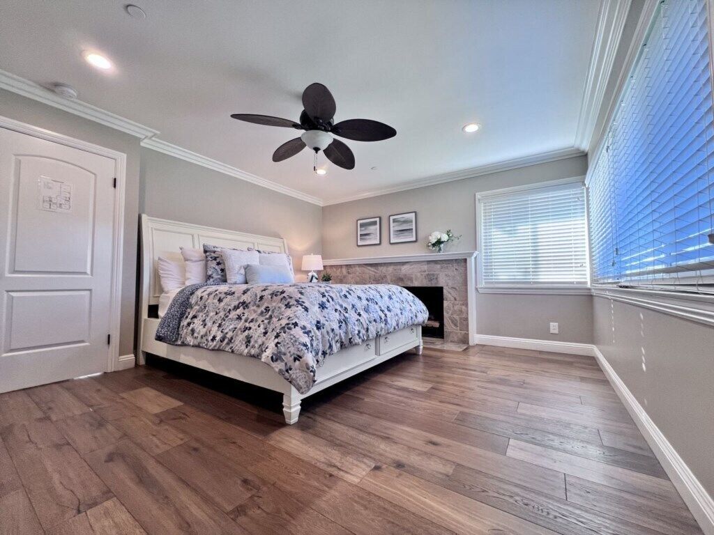 A bedroom with a bed, a ceiling fan, a fireplace, and a window with blinds.
