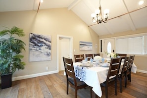 A dining area with a table set for four, surrounded by chairs, with a chandelier above and a large plant to the left.
