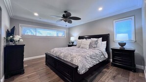 A bedroom with a bed, a ceiling fan, a nightstand, a dresser, and a window with blinds. - Snazzy 6 Bedroom 3 Bath Pool Home 1/2 Mile Walk to Disney (Anaheim)