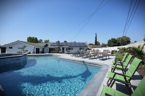 A swimming pool with lounge chairs, a building with solar panels, and a clear sky.