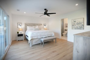 Une chambre à coucher avec un lit, un banc, un ventilateur de plafond, des lampes de chevet et un tableau au mur.
