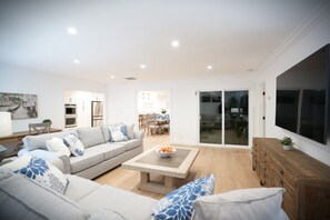 A modern living room with a sofa, coffee table, and a dining area in the background. - Awesome 5 Bedroom 3 Bath Pool Home With In-ground Jacuzzi (Orange)