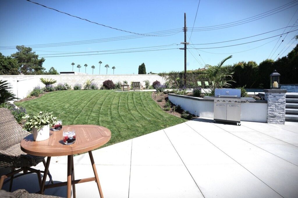 Une terrasse avec une table et des chaises, un barbecue et une pelouse bien entretenue.
